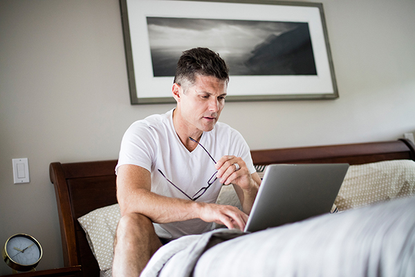 Man zit in bed terwijl hij naar de laptop kijkt